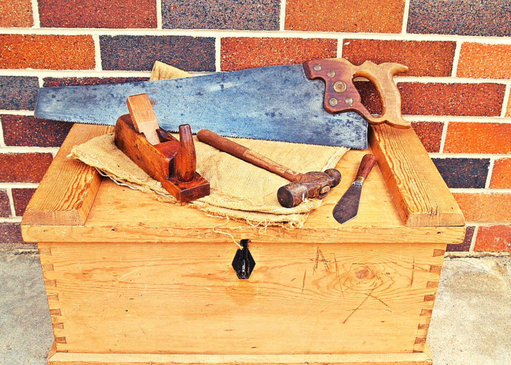 A rip saw, wooden hand plane, and some tools on a tool box