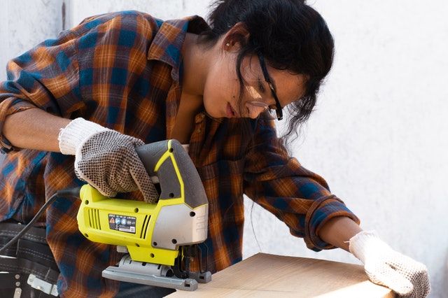 woman using a jigsaw to cut a piece of wood
